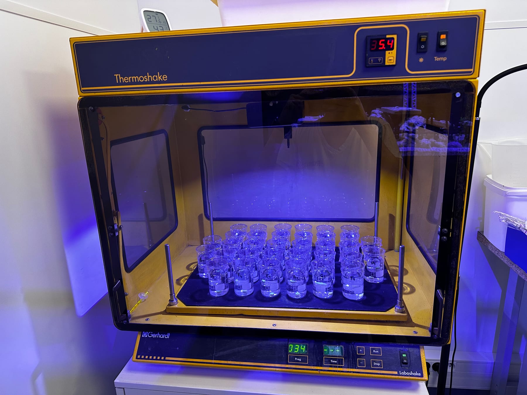 An open incubator-shaker holding the exposure beaker grid, with a digital temperature and timer readout