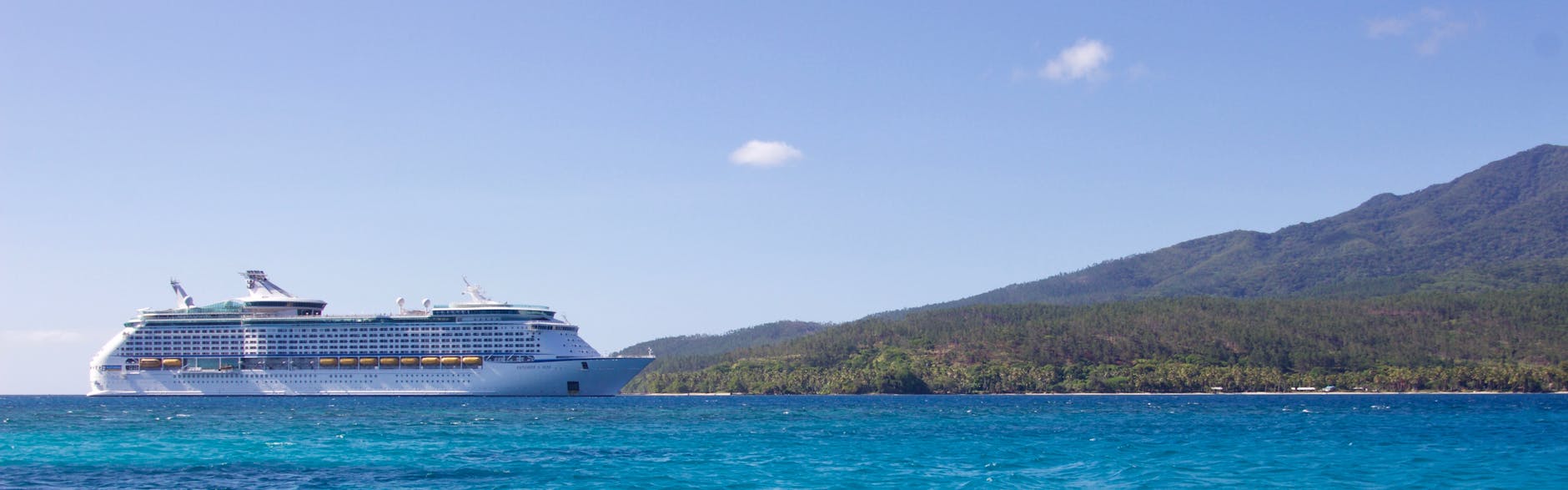 A cruise ship at anchor near a tropical island shoreline